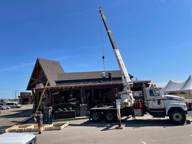 Crane lifting a skylight panel onto the roof of a patio