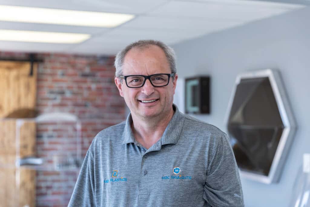 Man with glasses wearing a shirt with the Mac plastics & Skylights logo